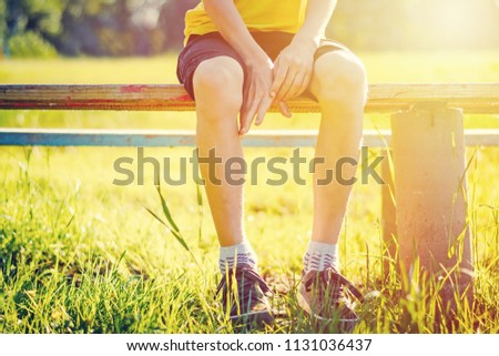 Bare feet of boy hang down from bench in summer park at sunset