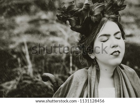 conceptual portrait of beautiful young woman with red lips, flowers in hair, sitting in wheel chair under rain. Black and white photo