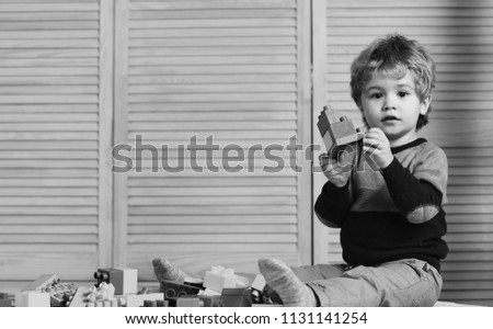 Childhood and educational activities concept. Boy plays with lego on wooden wall background, copy space. Toddler with curious face plays with colorful bricks. Kid builds of plastic blocks