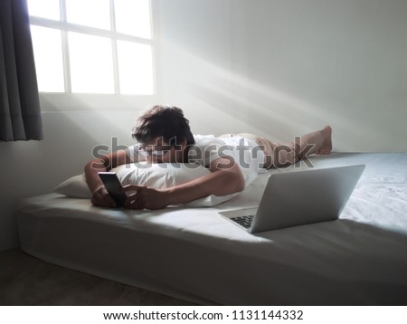 Young Asian man with mobile smart phone lying down on the bed in morning Royalty-Free Stock Photo #1131144332