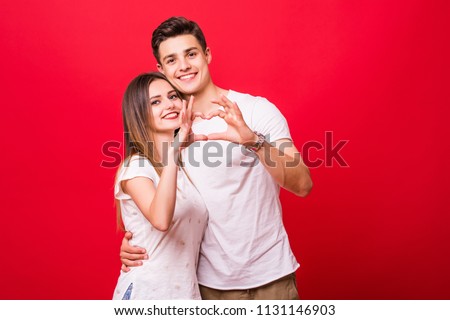 Two young smiling people in casual clothing hugging each other and making hear using their hands