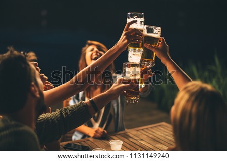 Group of friends drink beer on the terrace and toast during summer night Royalty-Free Stock Photo #1131149240