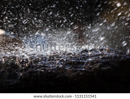 Wet stone in the rain. Rain water drop falling to the stone. Water is flowing and splashing around them.