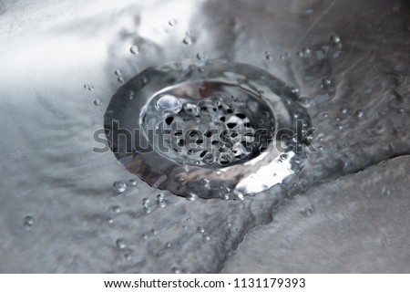 Close up of a metallic silver drain strainer in a sink with water flowing through the strainer in the kitchen pipes, to secure and protect the pipes from dirt and food leftovers or any kind of garbage Royalty-Free Stock Photo #1131179393