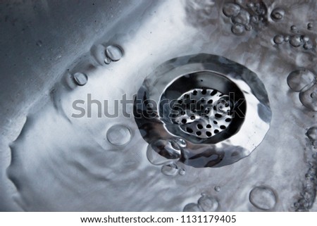 Close up of a metallic silver drain strainer in a sink with water flowing through the strainer in the kitchen pipes, to secure and protect the pipes from dirt and food leftovers or any kind of garbage Royalty-Free Stock Photo #1131179405