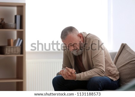 Depressed senior man sitting on sofa indoors Royalty-Free Stock Photo #1131188573