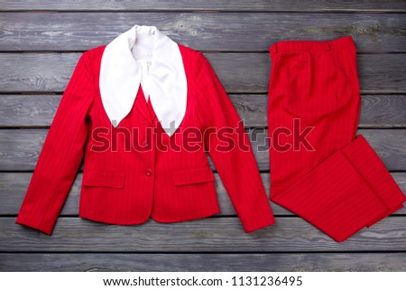 Red jacket with white collar. Folded trousers. Grey wooden surface background.