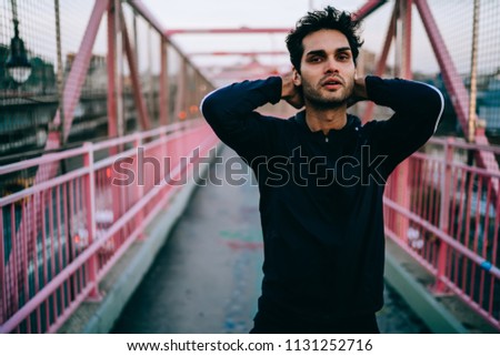 Half length portrait of tired male jogger looking at camera after doing exercises for training body muscles, fatigued sportsman in tracksuit recreating after running across city streets on leisure