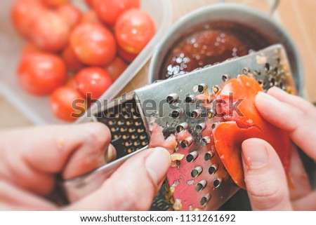 Personal perspective close-up view of hands grate tomatoes through a metal grater in kitchen. Royalty-Free Stock Photo #1131261692