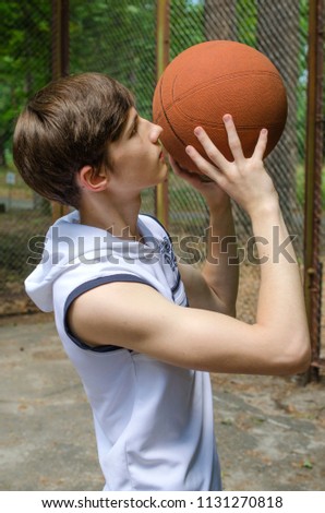 Teenager boy with a ball for basketball and in a sports shirt is playing basketball on the basketball court