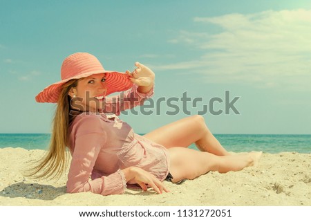 Young woman in big red hat lying on the sand at the beach. Summer vacation by the sea.