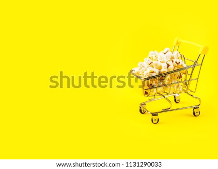 Popcorn in a shopping trolley on pink background top view