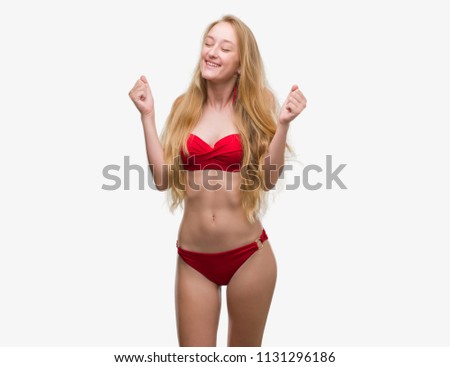 Blonde teenager woman wearing red bikini excited for success with arms raised celebrating victory smiling. Winner concept.