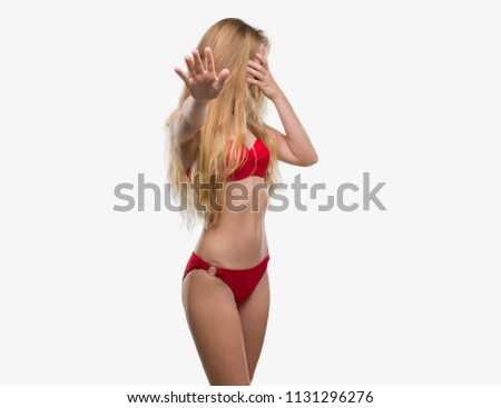 Blonde teenager woman wearing red bikini covering eyes with hands and doing stop gesture with sad and fear expression. Embarrassed and negative concept.