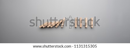 Wide cropped image of the outline of a businessman stopping the domino effect on gray background. Royalty-Free Stock Photo #1131315305