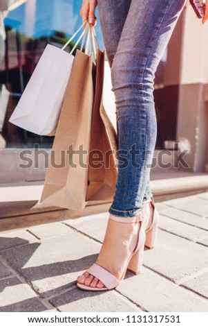Beautiful stylish young woman with shopping bags walking on city street in summer. Closeup of shoes and purchases. Sale