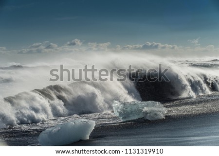 Waves crashing on a black sand shore in Iceland with Icebergs scattered around