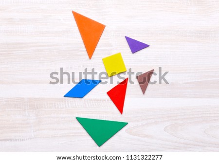 Colored geometric pieces of puzzle like triangles, square and parallelogram, are scattered on a light wooden background
