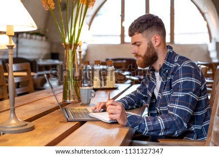 Casual business man or freelancer planning his work on notebook, working on laptop computer with smart phone, cup of coffee on table at coffee shop or home office.