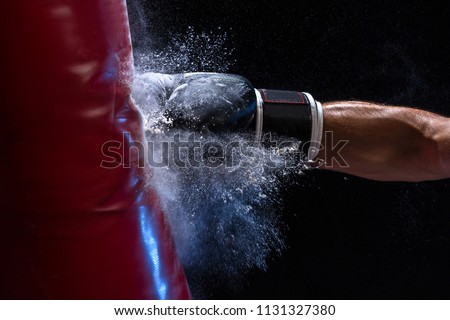 Close-up hand of boxer at the moment of impact on punching bag over black background Royalty-Free Stock Photo #1131327380