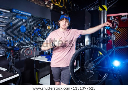 Small business and bicycle transport service. Portrait of a young man in a cap posing against the backdrop of a bicycle workshop and a tool for setting up and repairing..