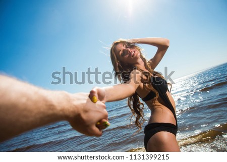 Girl holds her boyfriend's hand and pulls him to swim in the sea