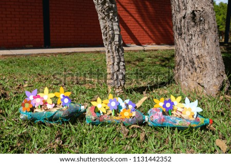 Close up of multi colored  paper flowers inside planters made of pet bottles in grass garden.