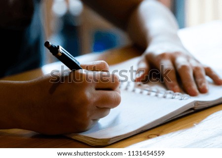 female hand with pencil writing on notebook at coffee shop.woman working by hand writing on letter paper on the wooden desk.woman hand writing.