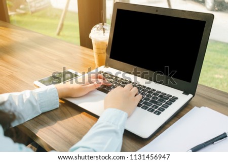 Close-up of business female working with laptop with blank black screen make a note document and smartphone in coffee shop like the background.