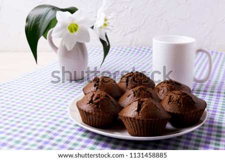 Chocolate muffins, coffee mug and white lily in rustic vase on the green purple checkered linen napkin