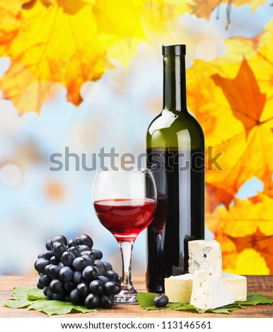 bottle, glass of red wine and assorted cheeses on a background of autumn leaves