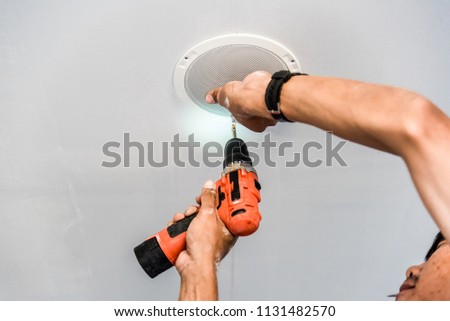 Technician is installing Ceiling Speaker in hotel by Cordless battery drill