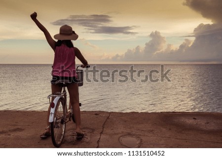 Asia teenager girl sit on the bike with both hand cheerful background sunset at the sea with copy space.