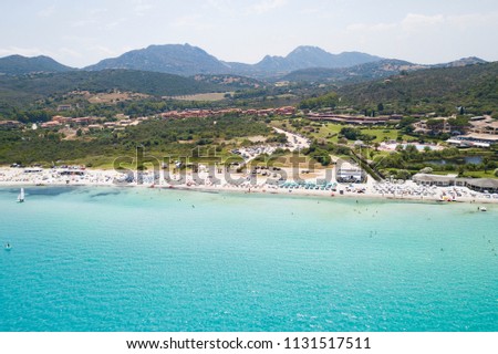 Aerial view of the amazing beach with turquoise and transparent sea. Colourful umbrellas  and people who swim in Sardinia, Mediterranean sea, Italy.