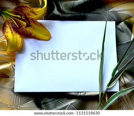 Romantic frame for a white sheet of paper from a bright lily and scarf with an abstract geometric pattern