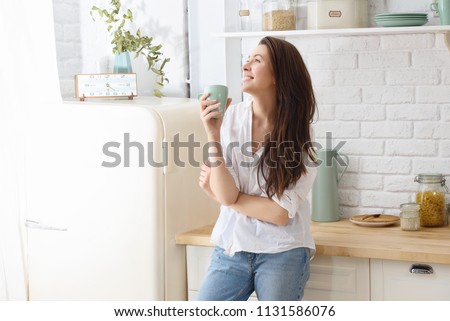 Young happy woman drinking coffee on the kitchen in the morning. Royalty-Free Stock Photo #1131586076