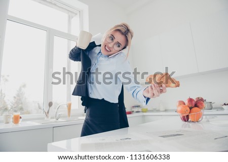Adorable busy attractive charming beautiful smiling lady office executive worker wearing spectacles in hurry early in the morning talking on the phone having a drink and croissant in kitchen Royalty-Free Stock Photo #1131606338