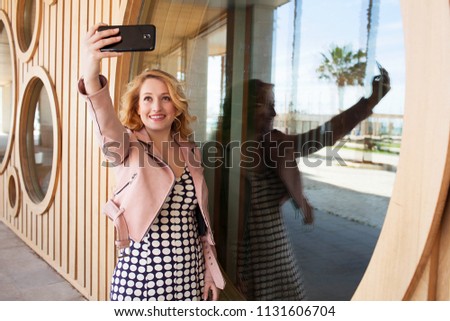 Beautiful young tourist solo traveller woman holding up smart phone taking selfies photos in sunny destination, outdoors. Smiling female using technology, leisure recreation lifestyle, exterior.