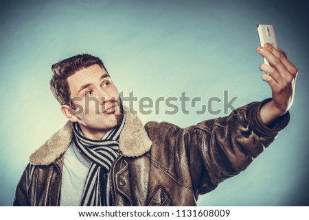Happy man with half shaved face beard hair taking selfie self photo with smartphone camera. Smiling handsome guy on blue. Skin care and hygiene. Instagram filter.