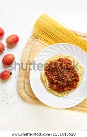 Spaghetti bolognese dish on chopping board with tomato and oregano on isolated white background. Top down view Vertical picture