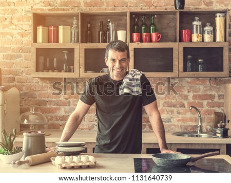 Young attractive man cutting cheese and talking on the phone in the kitchen