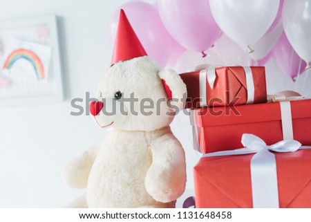 selective focus of teddy bear in cone with gift boxes and air balloons 