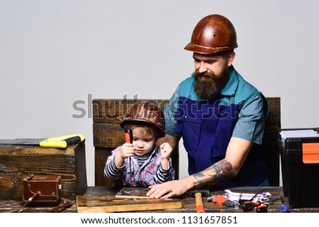 Father&son in workshop repairing. Father teaching little son to repair. Fatherhood&transfer of experience concept. Dad&son working with tools.Daddy with little son in protective helmet use screwdriver