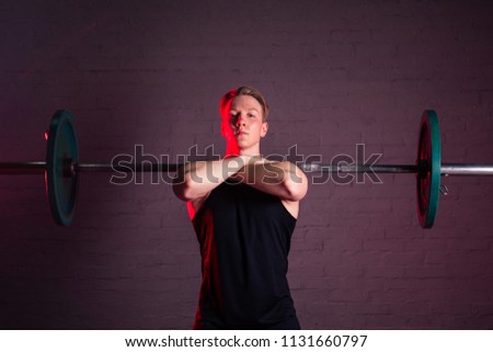 young handsome white man in black t-shirt is engaged with a barbell in the gym on a black brick background
