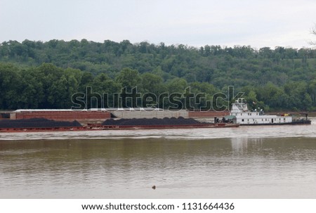 The barge pushing the coal up the flowing river on a cloudy day.