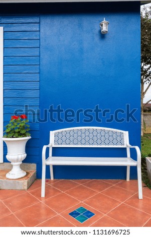 Front of blue house with long white chairs and flower pots and red roses.