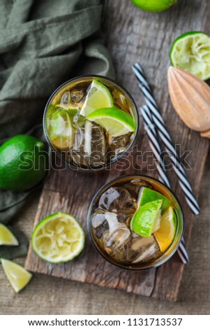 Food and drink, holidays party concept. Cuba libre or long island iced tea alcohol cocktail drink beverage, longdrink in a glass with straw, ice and lime on a dark table. Top view flat lay