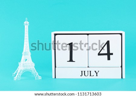 Miniature of the Eiffel Tower and wooden calendar on a blue background. The concept of the holiday is July 14, the Day of the Bastille.