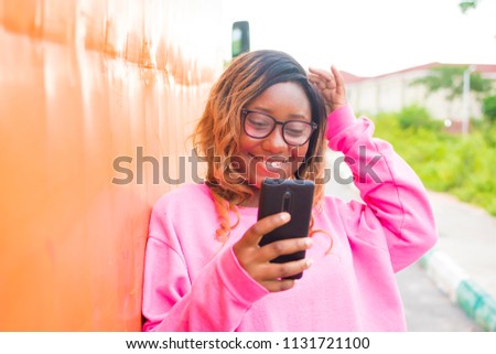 nigerian girl smiling while using her phone. black girl wearing pink smiling and using her phone 