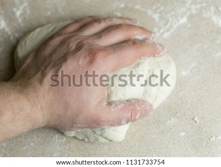 A man's hand kneads a dough.